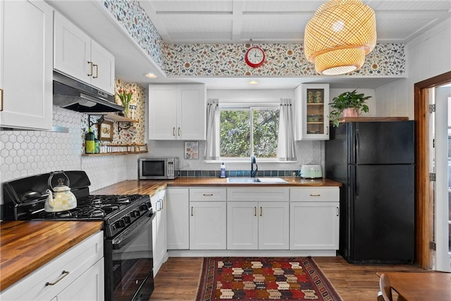 kitchen featuring wood counters, black appliances, under cabinet range hood, a sink, and open shelves