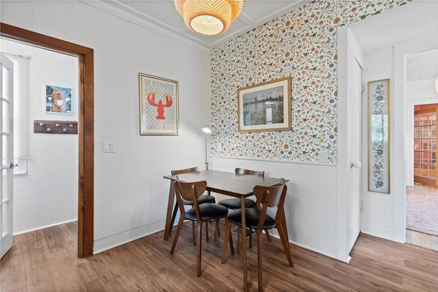 dining room with wood finished floors, wallpapered walls, plenty of natural light, wainscoting, and ornamental molding