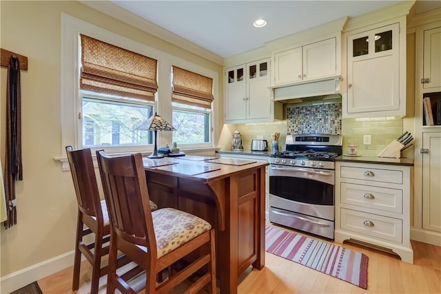kitchen with gas stove, under cabinet range hood, backsplash, glass insert cabinets, and light wood finished floors
