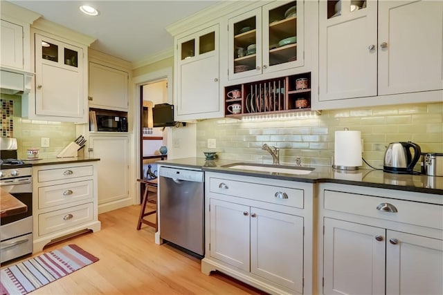 kitchen with appliances with stainless steel finishes, a sink, dark countertops, backsplash, and light wood-type flooring