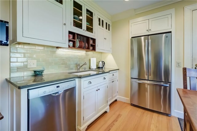 kitchen with stainless steel appliances, a sink, light wood-type flooring, decorative backsplash, and white cabinetry