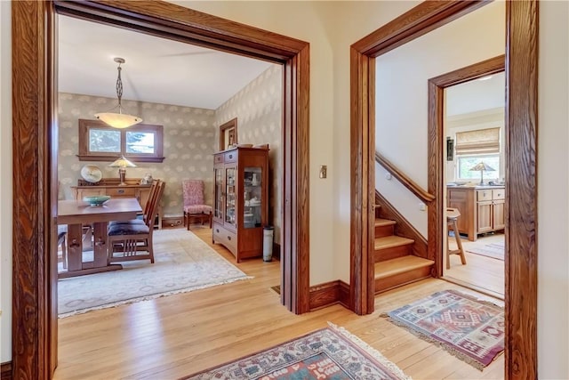 hallway with wallpapered walls, light wood-style flooring, stairway, and baseboards