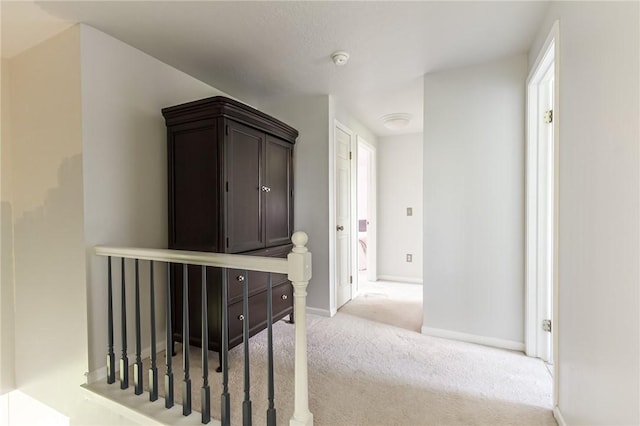 hall with carpet floors, baseboards, and an upstairs landing