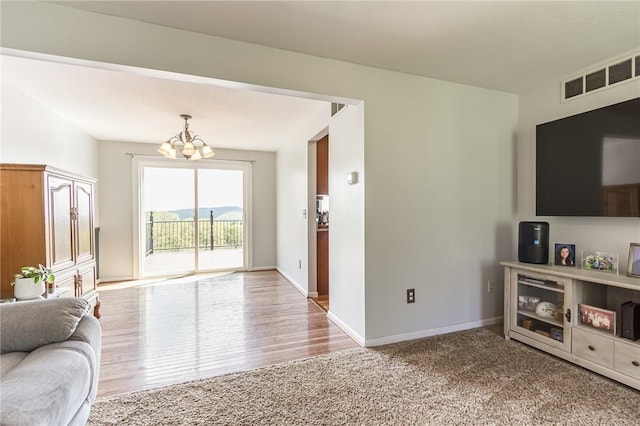 carpeted living area with a chandelier, baseboards, and wood finished floors
