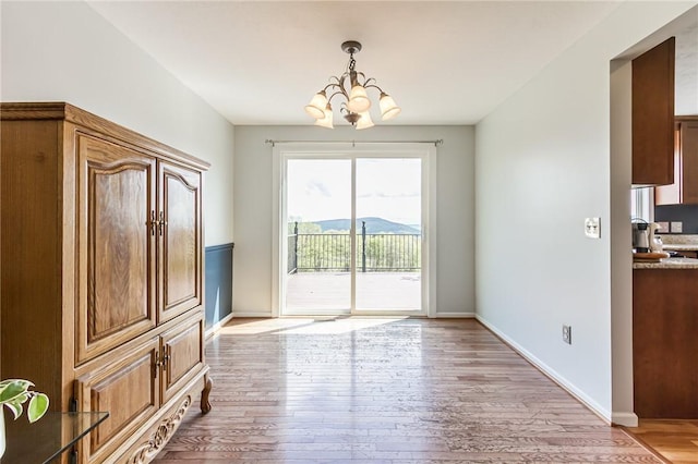 unfurnished dining area featuring a chandelier, light wood-style flooring, and baseboards