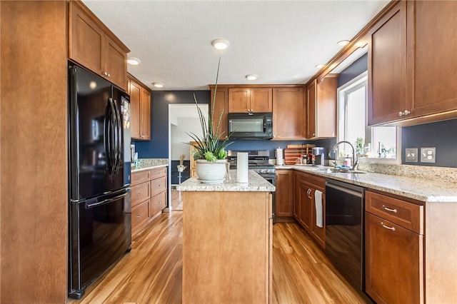 kitchen featuring black appliances, a sink, light wood-style floors, a kitchen island, and light stone counters