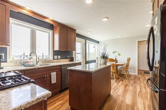 kitchen with freestanding refrigerator, dishwasher, a sink, a kitchen island, and light wood-style flooring