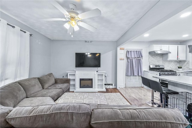 living room featuring light wood finished floors, ceiling fan, recessed lighting, and baseboards
