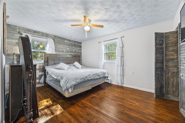 bedroom featuring a baseboard radiator, wood finished floors, baseboards, an accent wall, and a ceiling fan
