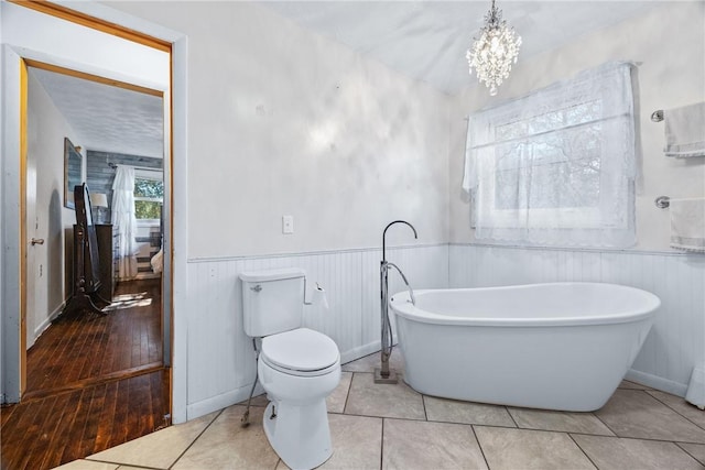 full bath with toilet, a freestanding tub, wainscoting, a chandelier, and baseboards