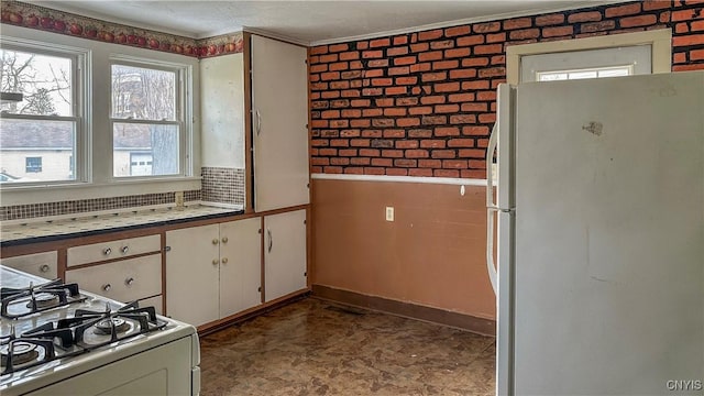 kitchen with white appliances, white cabinetry, brick wall, crown molding, and tile patterned floors