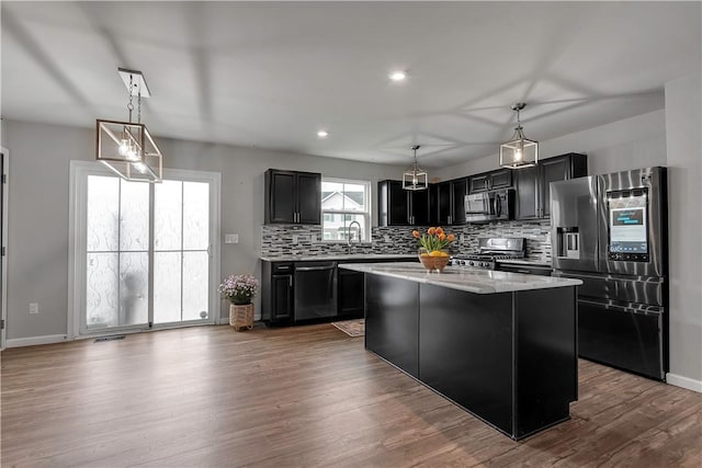 kitchen with stainless steel appliances, dark cabinetry, backsplash, a kitchen island, and a sink