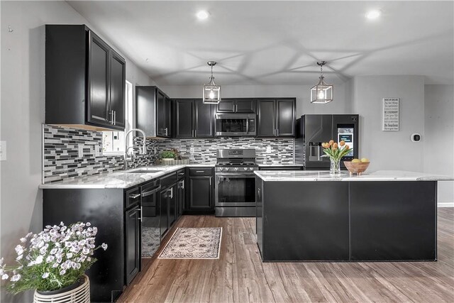 kitchen featuring stainless steel appliances, dark cabinetry, a sink, a center island, and wood finished floors