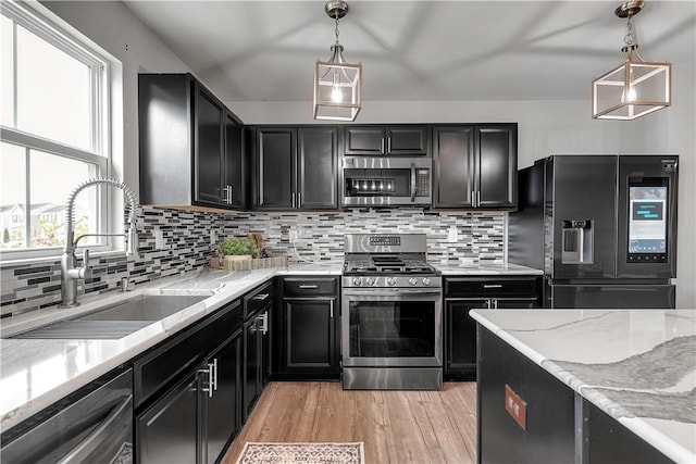 kitchen featuring stainless steel appliances, a sink, dark cabinets, and plenty of natural light