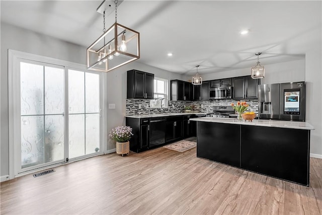 kitchen with appliances with stainless steel finishes, dark cabinetry, light wood finished floors, decorative backsplash, and a chandelier