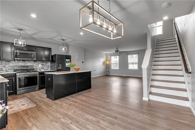 kitchen with appliances with stainless steel finishes, light countertops, a center island, baseboards, and decorative backsplash