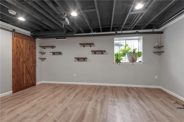 below grade area featuring a barn door, light wood-style flooring, and baseboards