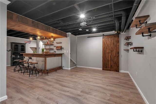 indoor dry bar featuring a barn door, wood finished floors, and baseboards