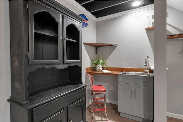 bar area with a sink, baseboards, and light wood-type flooring