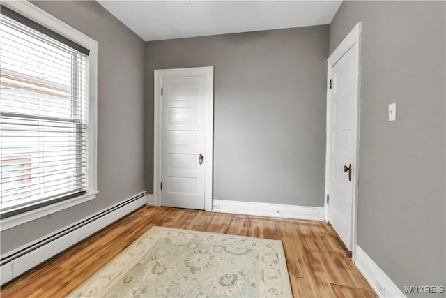 spare room with a baseboard heating unit, healthy amount of natural light, light wood-style flooring, and baseboards