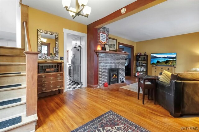 living area featuring wood finished floors, a chandelier, and a brick fireplace