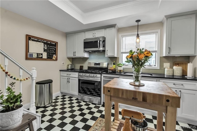 kitchen with appliances with stainless steel finishes, light floors, a raised ceiling, pendant lighting, and ornamental molding