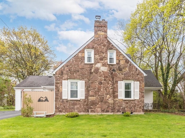 view of home's exterior featuring stone siding, a chimney, a yard, and a shingled roof