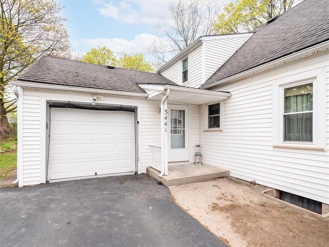 doorway to property with a garage, a shingled roof, and driveway