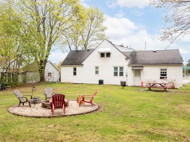 rear view of property featuring an outdoor fire pit, a shingled roof, a lawn, and cooling unit