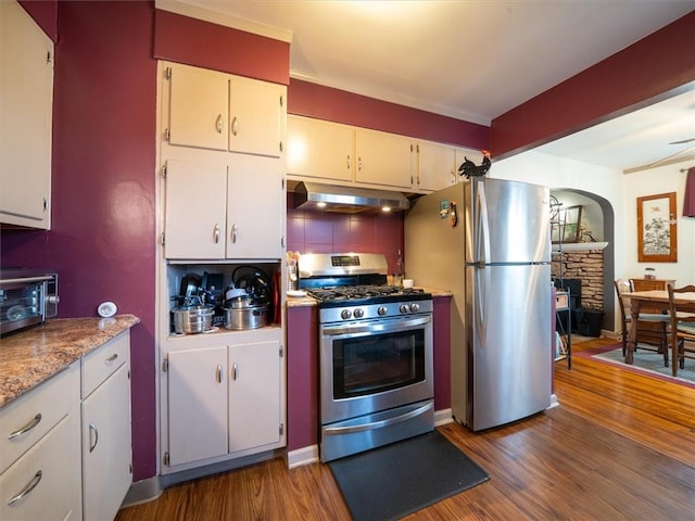 kitchen featuring stainless steel appliances, under cabinet range hood, arched walkways, dark wood-style floors, and decorative backsplash