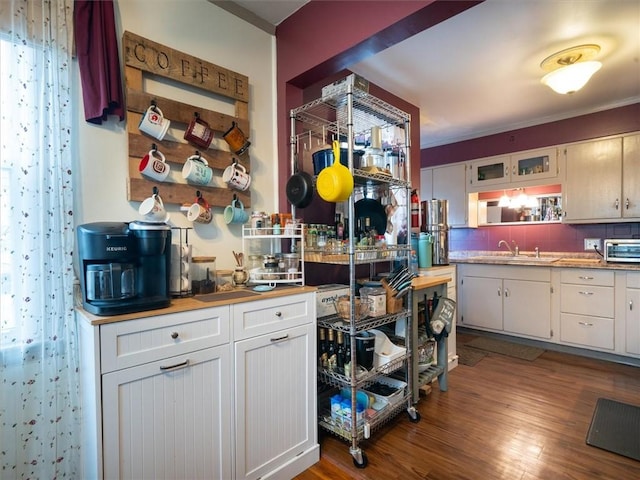 kitchen featuring a sink, white cabinetry, dark wood-type flooring, decorative backsplash, and ornamental molding