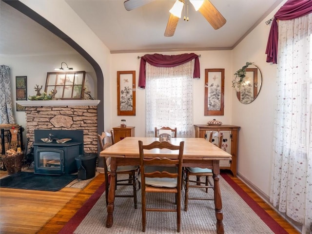 dining room featuring wood finished floors, a wood stove, ceiling fan, and baseboards
