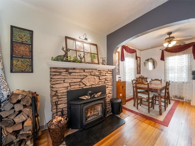 living area with hardwood / wood-style flooring, arched walkways, ceiling fan, baseboards, and a wood stove