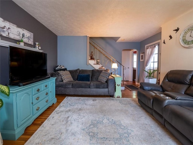 living area with stairway, a textured ceiling, dark wood-style floors, and arched walkways