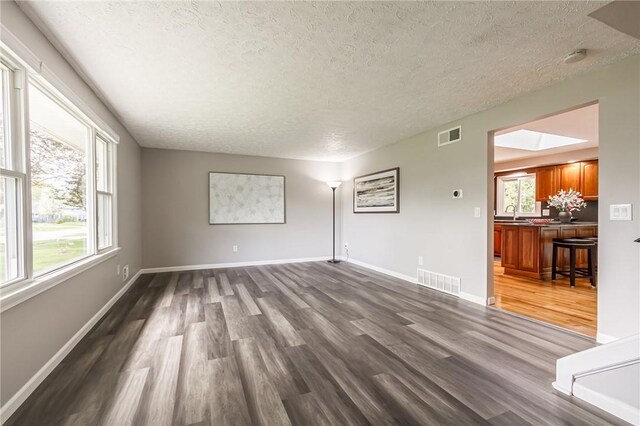 unfurnished living room featuring a textured ceiling, dark wood-style floors, baseboards, and a sink