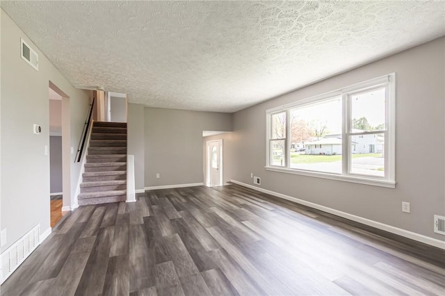 unfurnished living room with dark wood-type flooring, a textured ceiling, stairway, and baseboards
