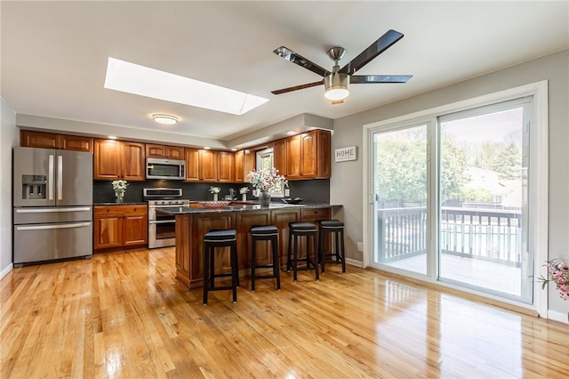 kitchen with appliances with stainless steel finishes, a skylight, dark countertops, brown cabinets, and light wood finished floors
