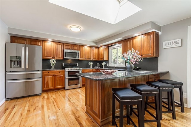 kitchen featuring stainless steel appliances, light wood finished floors, a peninsula, brown cabinets, and backsplash