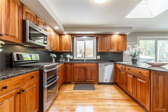 kitchen featuring stainless steel appliances, a sink, brown cabinetry, and recessed lighting