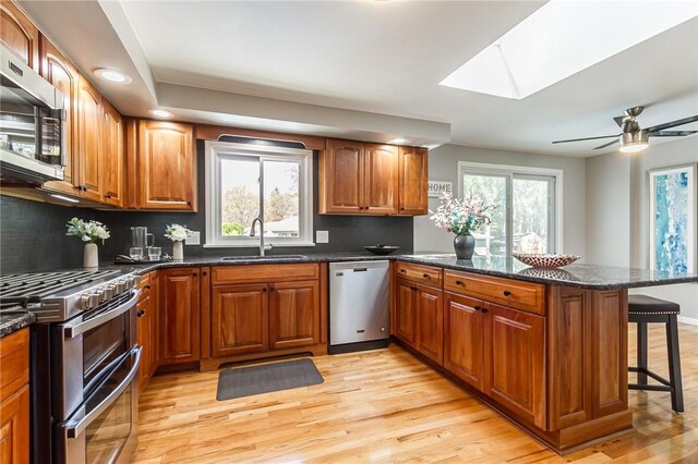 kitchen featuring appliances with stainless steel finishes, a sink, a peninsula, a skylight, and a breakfast bar