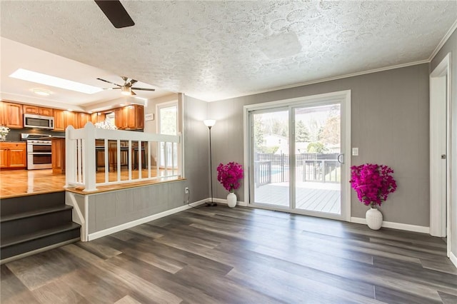 unfurnished living room featuring ceiling fan, baseboards, wood finished floors, a textured ceiling, and crown molding