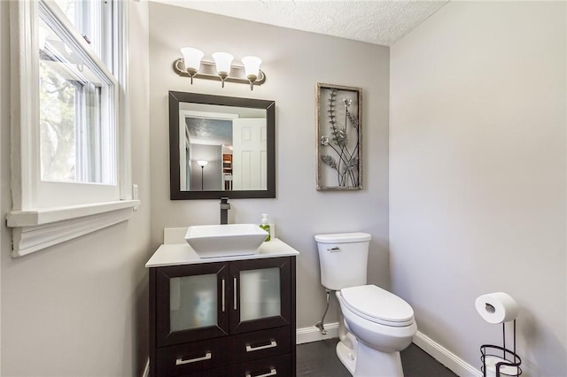 half bathroom featuring toilet, baseboards, vanity, and a textured ceiling