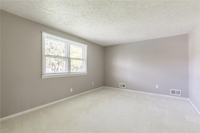spare room featuring light carpet, baseboards, and a textured ceiling