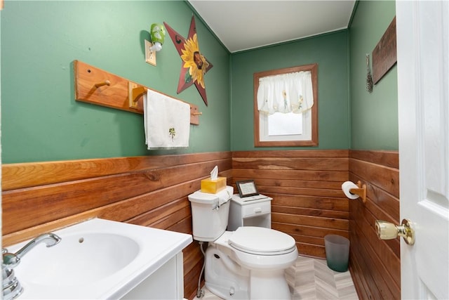 half bath featuring toilet, a sink, wooden walls, and wainscoting