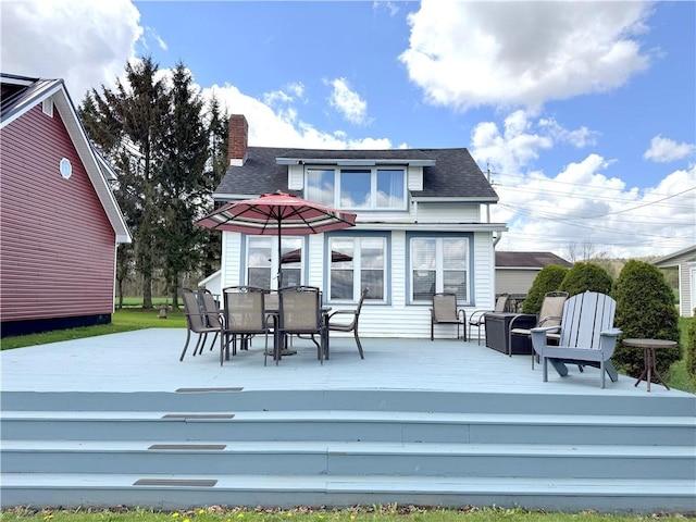 back of property featuring a wooden deck, outdoor dining area, a chimney, and a shingled roof
