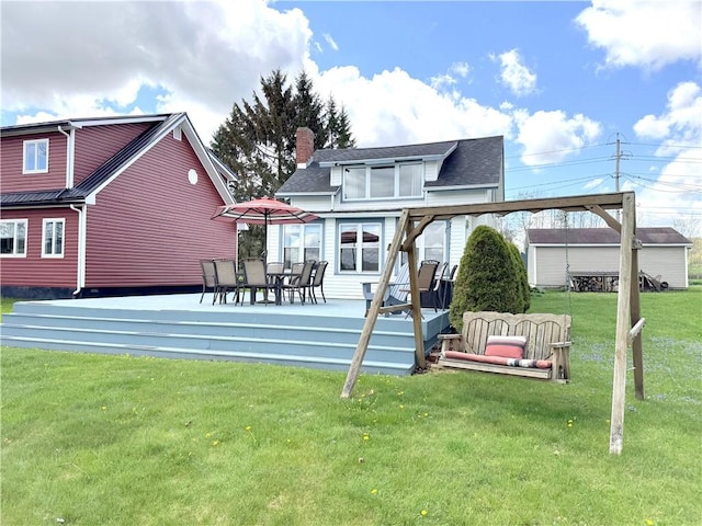 back of house featuring a yard, a chimney, a deck, and roof with shingles