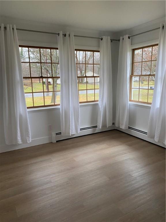 spare room featuring healthy amount of natural light, wood finished floors, and a baseboard heating unit