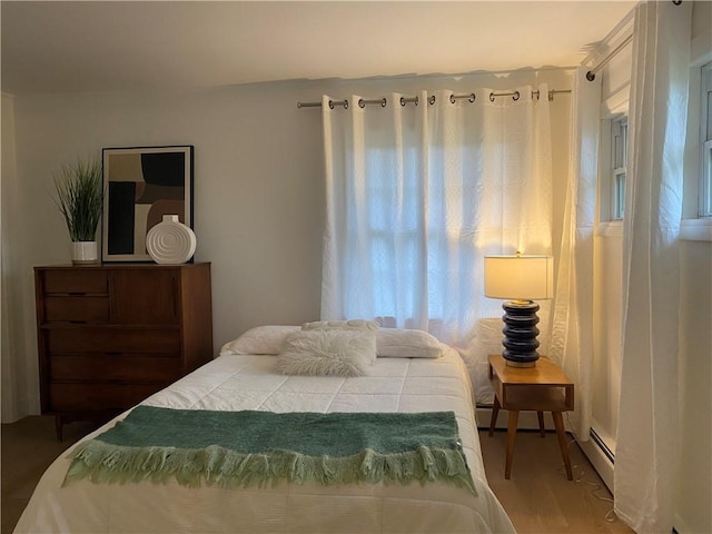 bedroom with wood finished floors and a baseboard heating unit