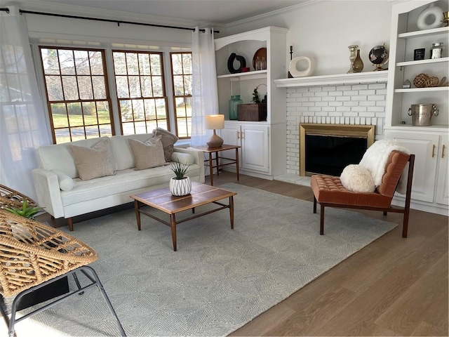 living area with wood finished floors, ornamental molding, built in features, and a fireplace