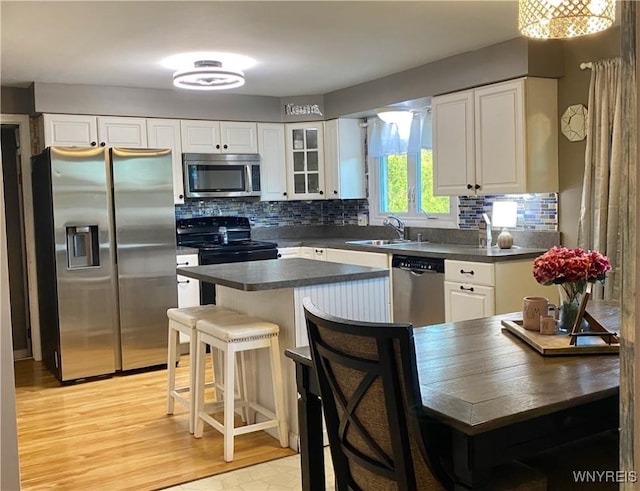 kitchen featuring stainless steel appliances, dark countertops, a sink, and white cabinets